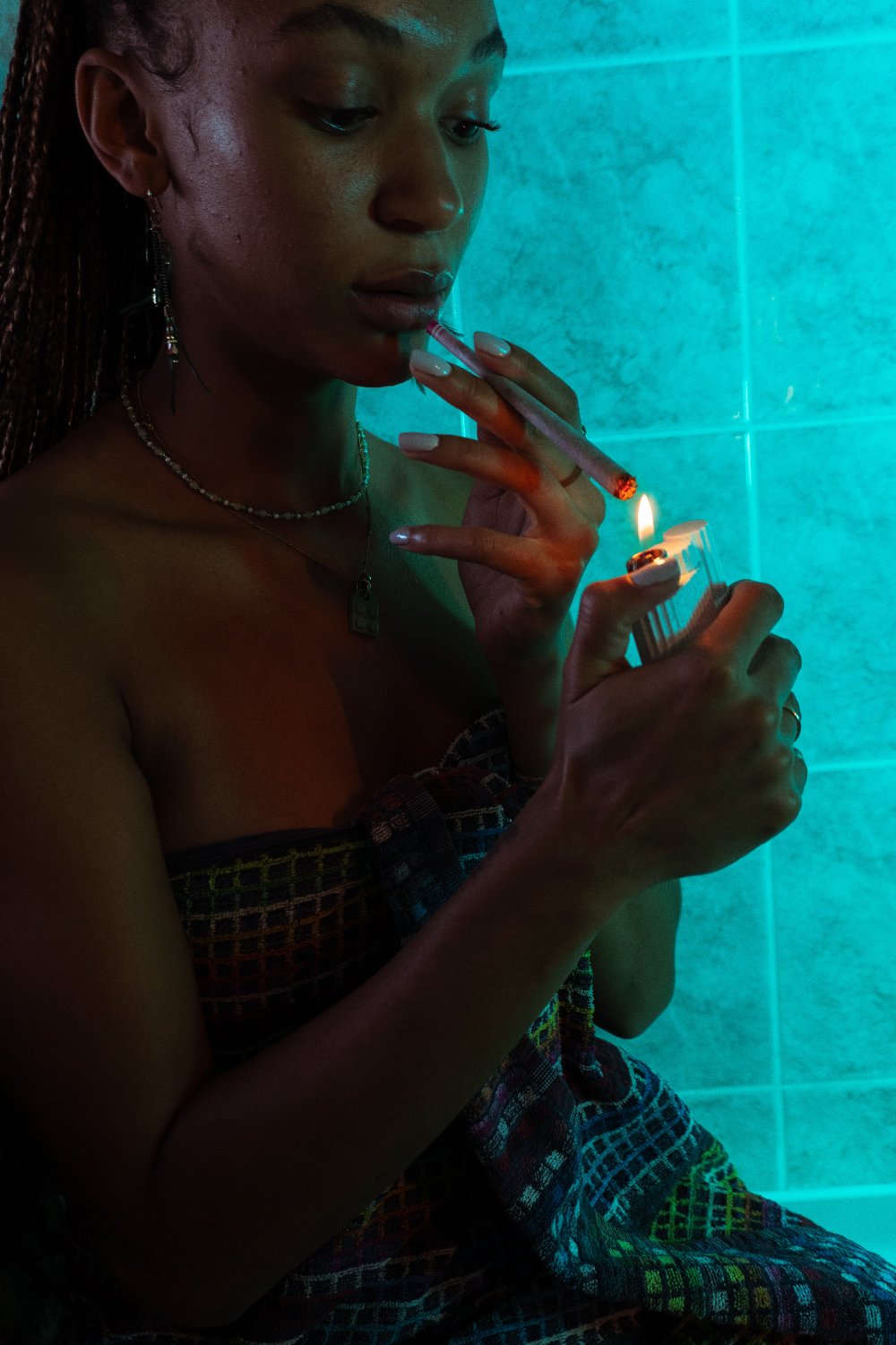 Une femme allume un joint avec un Clipper devant des carreaux turquoise